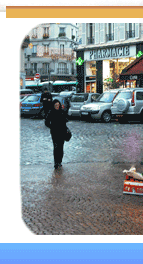 Woman walking on rainy cobblestone street in Rue Mouffetard, Paris, near pharmacy with classic buildings and parked cars